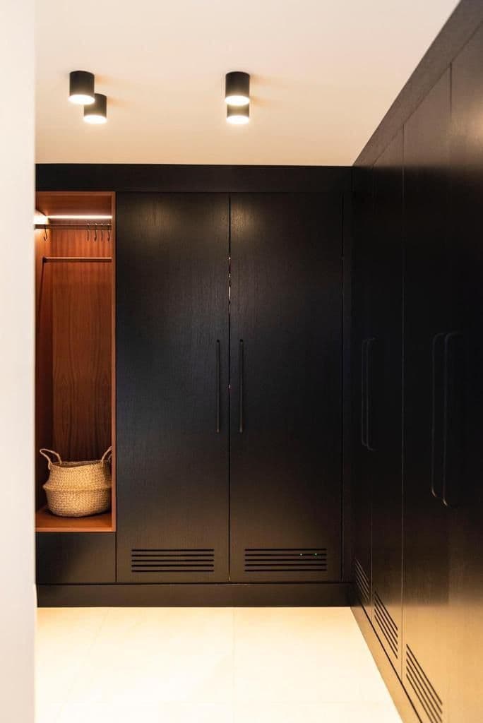 Dark fitted wardrobes with brass handles either side of a walk in wardrobe