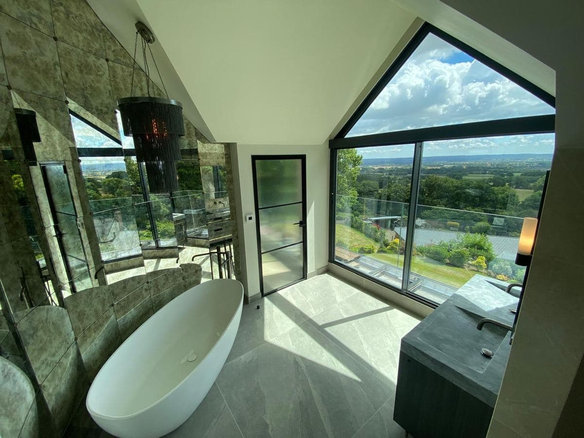 Bathroom with a freestanding bath, stone clad wall and a long view