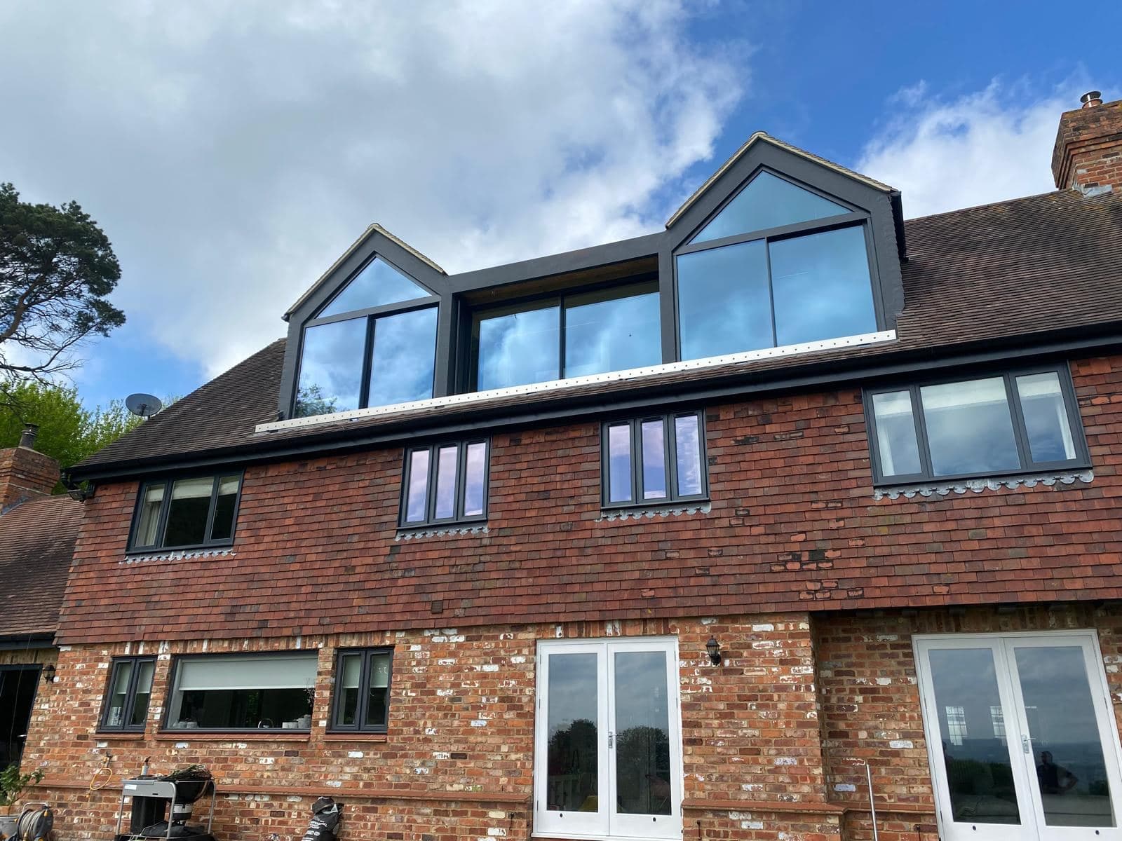 Rear of the country house with two new gabled dormers and a glazed section between them above the original brick and tile