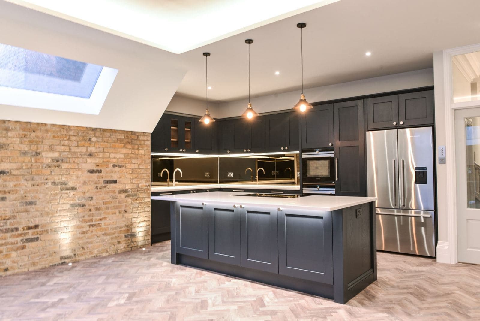 Navy kitchen with an island, exposed brick wall and a rooflight over herringbone flooring