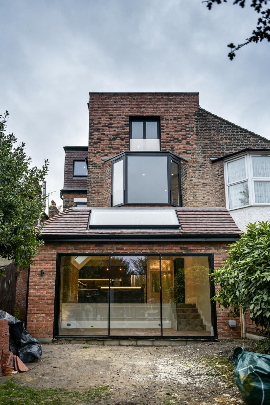 Rear of the finished house in brick, with a glazed bay, a loft extension above and sliding doors across the ground floor